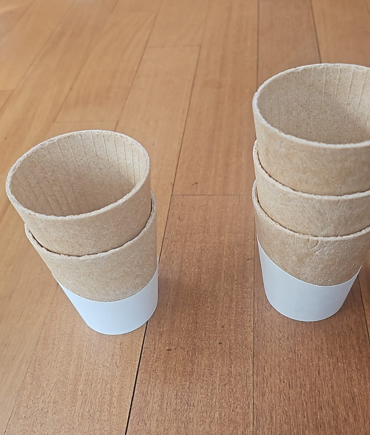 Two sets of cardboard cups with white bases on a wooden surface