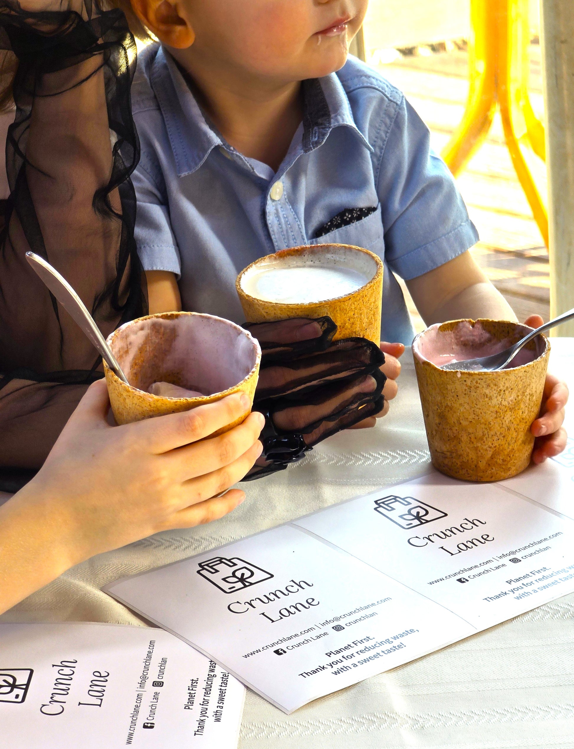 Child and adult sitting at a table with wooden cups and a menu titled 'Crunch Lane'.