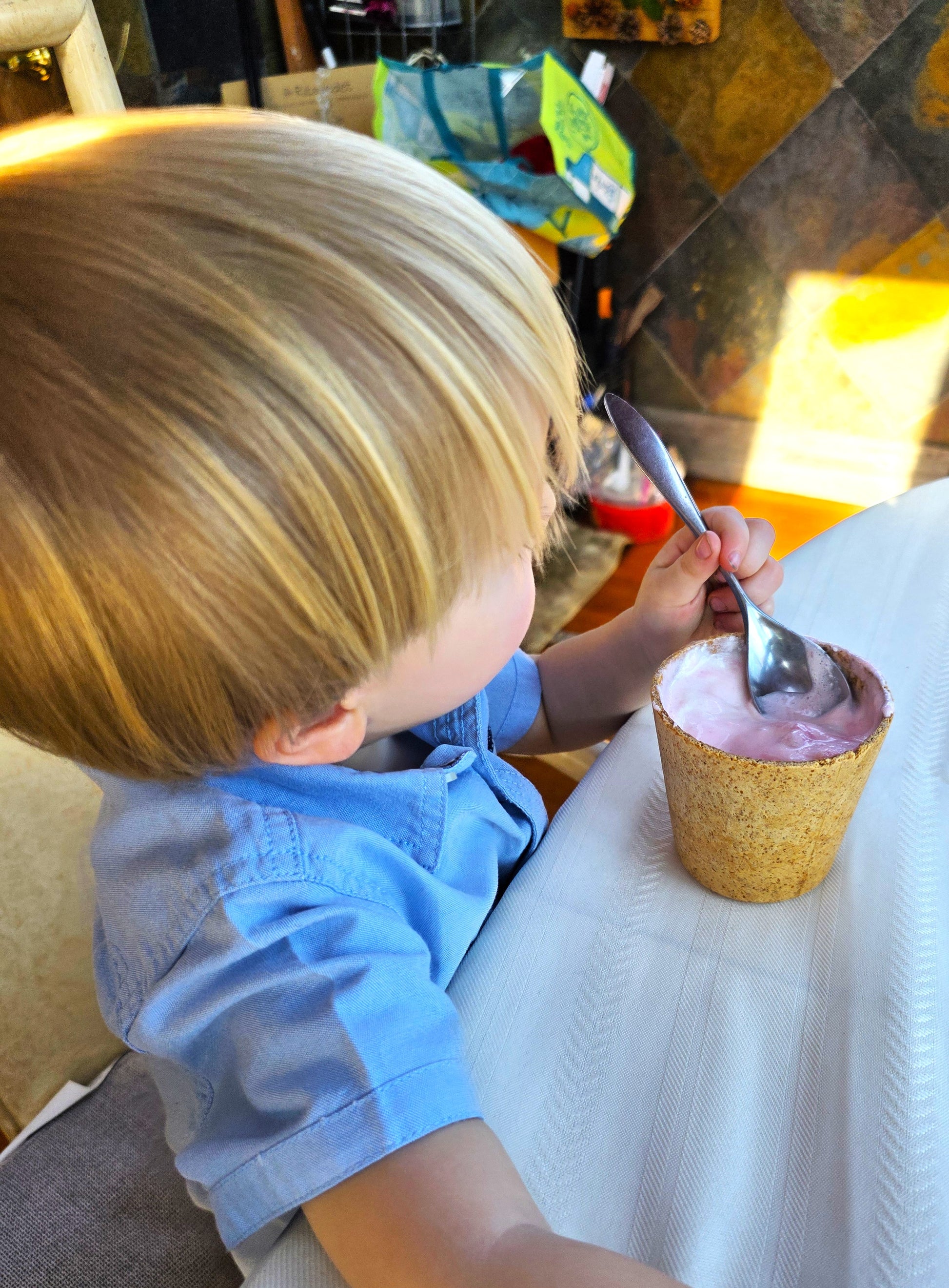Child in a blue shirt eating ice cream from a waffle cone with a spoon.